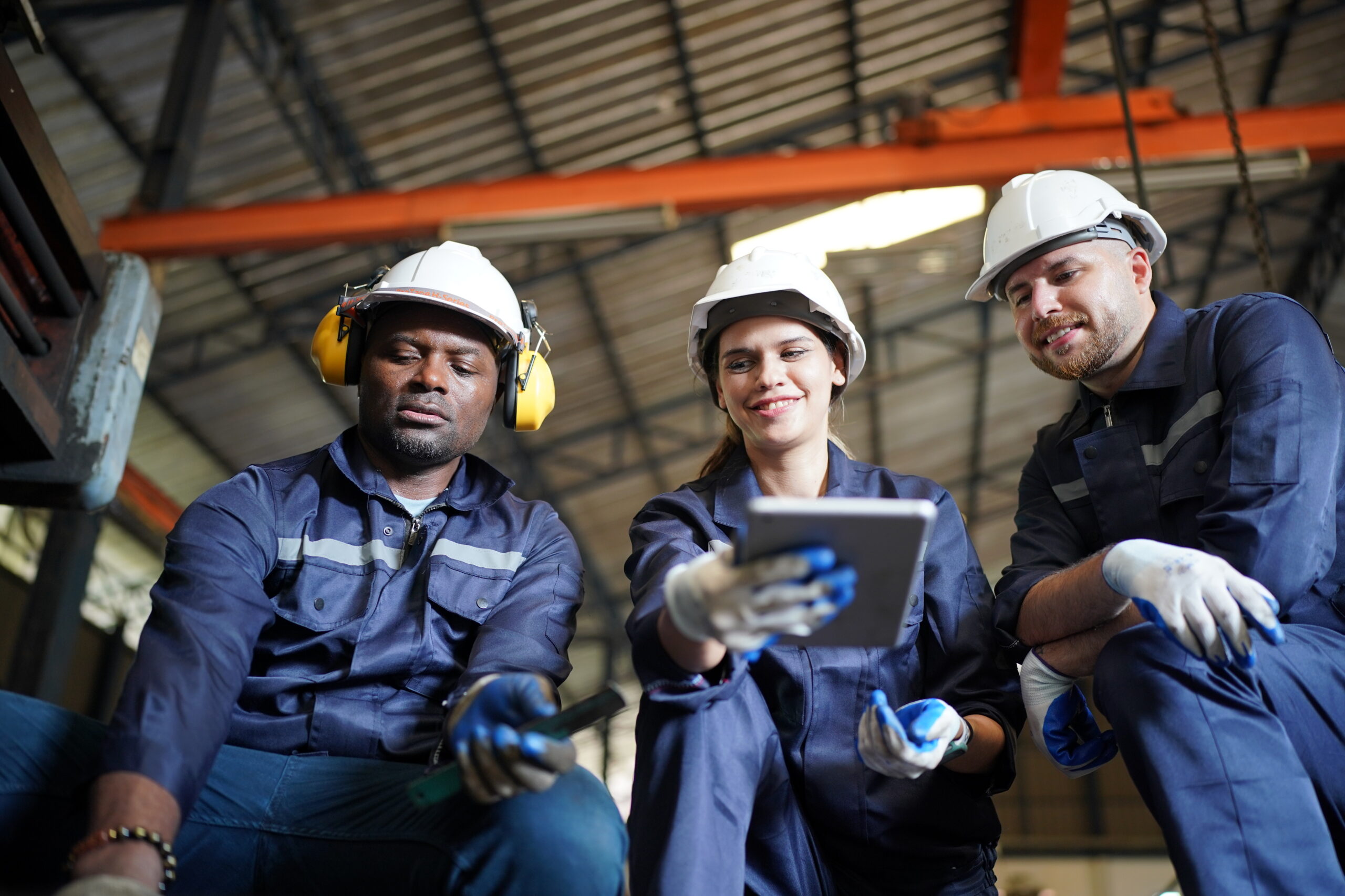 Young successful technician or repairman of industrial machines in safety helmet and workwear standing in large garage or workshop
